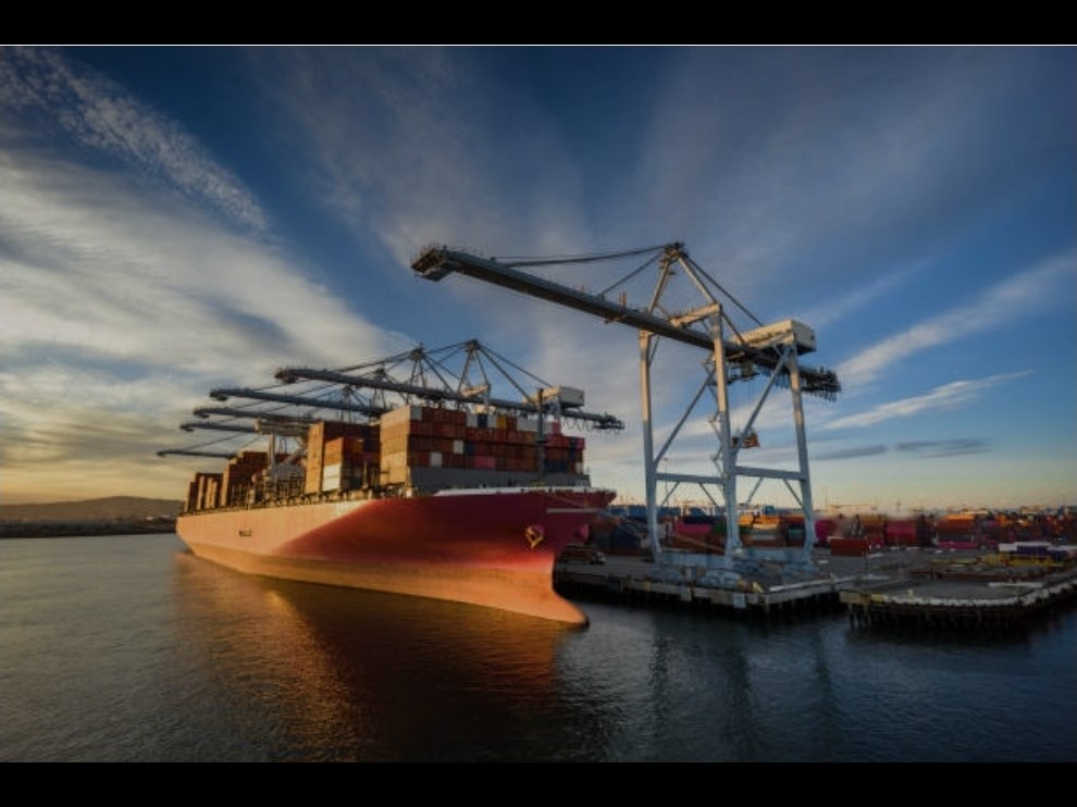 Buque portacontenedores atracado bajo las grúas del puerto al atardecer